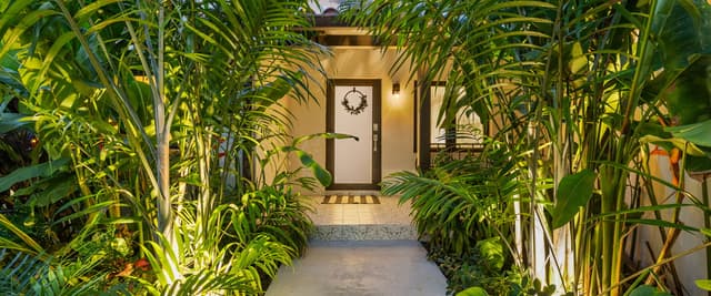 Backyard with lounge chairs, fire pit, gravel seating area, pool loungers, gray house, palm trees, and dramatic sunset sky